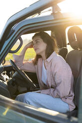 Thoughtful woman leaning on steering wheel in car during sunset - AFVF07587