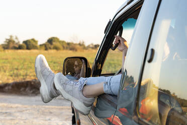 Legs of young woman on car window during sunset - AFVF07603