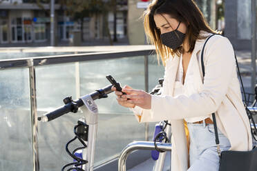 Young female entrepreneur doing contactless payment while standing at bicycle parking station - AFVF07629