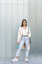 Stilvolle Unternehmerin mit Hand in der Tasche vor einer Glaswand stehend - AFVF07638