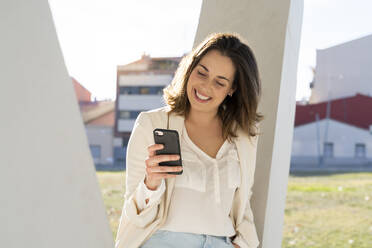 Smiling businesswoman using smart phone in city on sunny day - AFVF07657