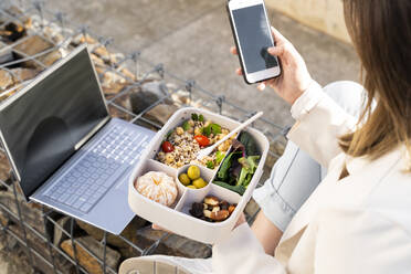 Female entrepreneur using smart phone while holding reusable lunch box - AFVF07664