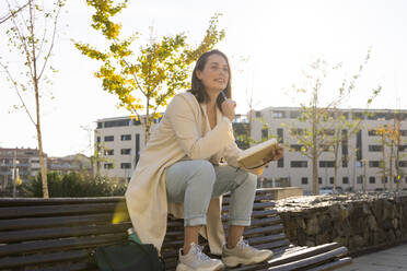 Thoughtful businesswoman sitting on bench with book - AFVF07668