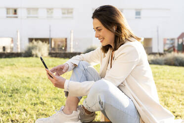 Lächelnde Unternehmerin, die ein Smartphone benutzt, während sie im Garten sitzt - AFVF07695