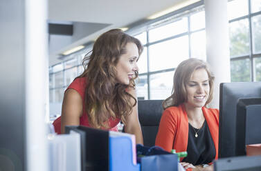 Female coworkers discussing while looking at computer in office - AJOF00640