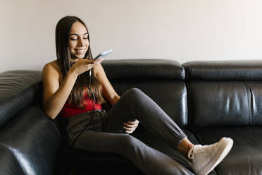 Smiling teenage girl talking on mobile phone while sitting on sofa at home - EGAF01082