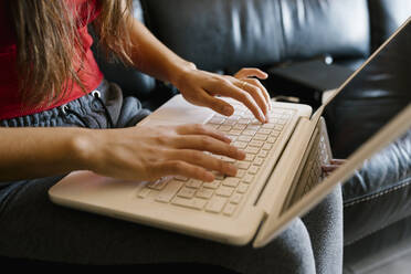 Teenage girl using laptop while sitting on sofa at home - EGAF01084