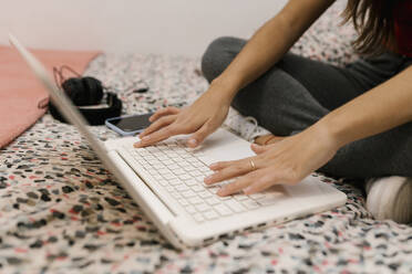 Teenage girl trying on laptop while sitting on bed - EGAF01089