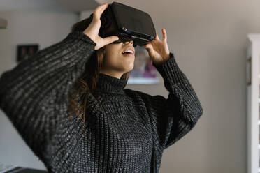 Teenage girl using virtual reality simulator while standing at home - EGAF01096