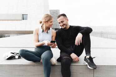 Athlete smiling while using mobile phone sitting outdoors - FMOF01221