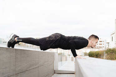 Young man doing push-ups on rooftop retaining wall - FMOF01222