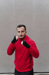 Confident sportsman with bandaged hand boxing while standing against wall - FMOF01235