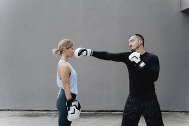 Sportsman teaching boxing to woman while standing against wall - FMOF01241