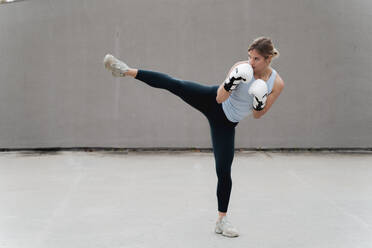 Frau mit Boxhandschuh übt Kickboxen an der Wand - FMOF01248