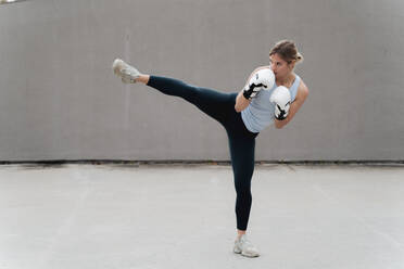 Woman with boxing glove practicing kickboxing against wall - FMOF01248