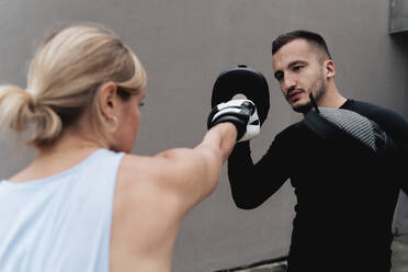 Sportlerin im Sparring mit einem Mann, der an der Wand steht - FMOF01252