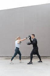 Ein Sportler bringt einer Frau das Boxen bei, während er an der Wand steht - FMOF01253