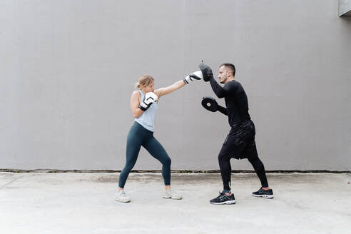 Sportlerin beim Boxen mit einem Mann, der an der Wand steht - FMOF01254