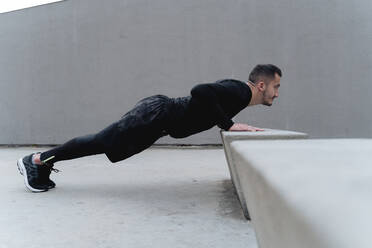 Male athlete doing push-up while exercising against wall - FMOF01257