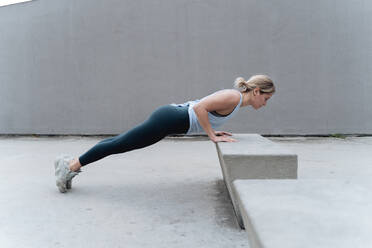 Sportswoman doing push-ups while exercising against wall - FMOF01258