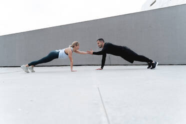 Young couple giving high-five while doing plank against wall - FMOF01264