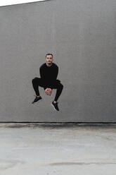 Young man jumping against wall - FMOF01269