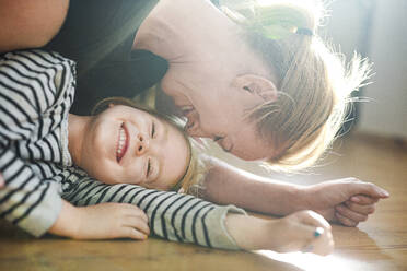 Happy mother playing with daughter while lying on floor at home - MKF00024