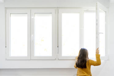 Girl opening window and looking out while standing at home - OCMF01855