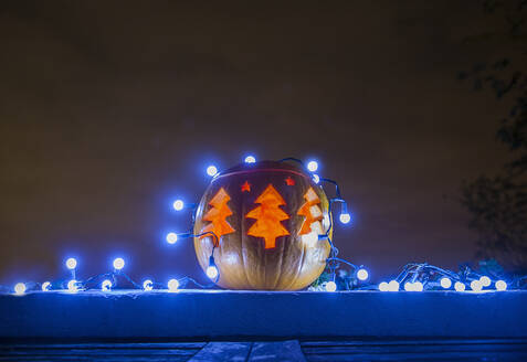 Jack o lantern decorated with blue Christmas lights glowing outdoors at night - AJOF00665