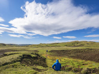 Wolken über einem männlichen Wanderer, der im Gras sitzt und die abgelegene isländische Landschaft bewundert - LAF02570