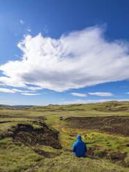 Wolken über einem männlichen Wanderer, der im Gras sitzt und die abgelegene isländische Landschaft bewundert - LAF02571