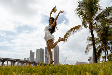 Fröhliche junge Frau springt über Gras gegen den Himmel - MAUF03595