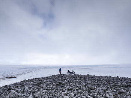 Männlicher Tourist erkundet auf dem Land stehend den bewölkten Himmel, Langjokull, Island - LAF02615