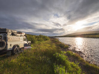 Geländewagen vor bewölktem Himmel bei Sonnenuntergang, Hraunfossar, Island - LAF02618