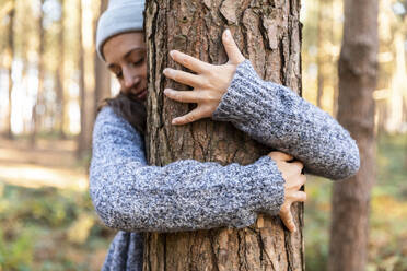 Female explorer embracing tree trunk while hiking in Cannock Chase woodland - WPEF03656