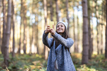 Lächelnde Wanderin, die ein Selfie mit ihrem Smartphone macht, während sie im Wald von Cannock Chase steht - WPEF03667