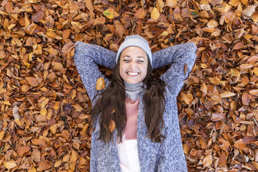 Happy female hiker with hands behind head lying down on autumn leaves in Cannock Chase forest - WPEF03681