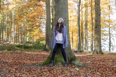 Female explorer standing against tree trunk in Cannock Chase forest - WPEF03683