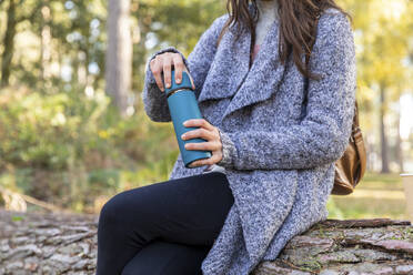 Female hiker holding insulated drink container while sitting in Cannock Chase woodland - WPEF03695