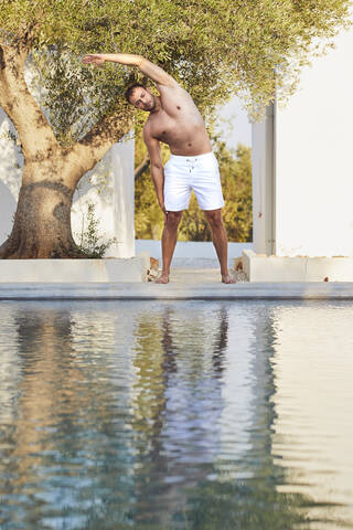 Young man doing stretching exercise at poolside stock photo