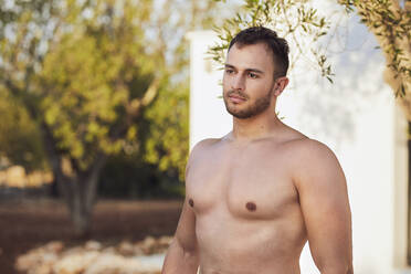 Nachdenklicher junger Mann ohne Hemd im Hinterhof stehend - UKOF00079