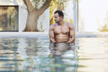 Thoughtful young man looking away while standing in swimming pool - UKOF00082