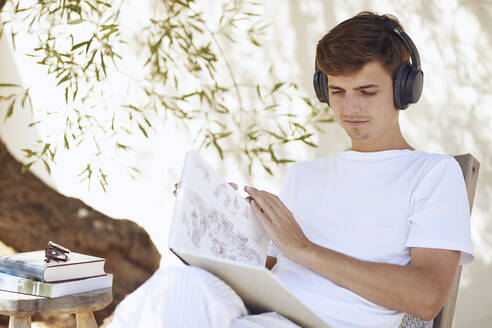 Junger Mann liest ein Buch und hört Musik an der Wand - UKOF00095
