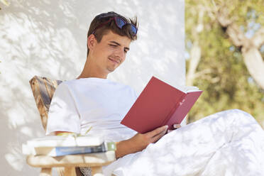 Young man reading book in backyard - UKOF00099