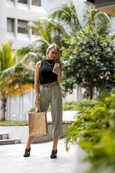 Frau mit Einkaufstüten, die auf dem Gehweg steht und ein Mobiltelefon benutzt - MAUF03611