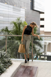 Mittlere erwachsene Frau mit Einkaufstasche, die nach unten schaut, während sie am Geländer steht - MAUF03619