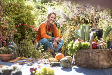 Lächelnde Frau, die im Garten sitzend Obst und Gemüse erntet - HHF05600