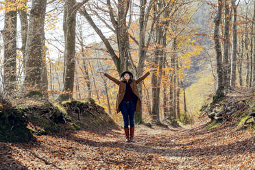 Carefree woman standing with arms outstretched on footpath at forest - FMOF01283