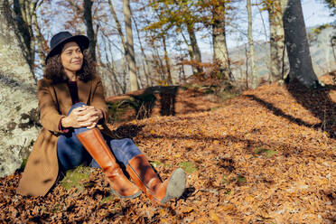 Smiling woman sitting under tree in forest - FMOF01285