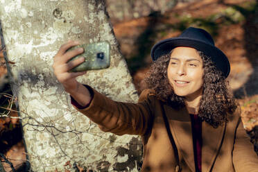 Frau lächelnd bei der Aufnahme von Selfie durch Handy im Wald - FMOF01288